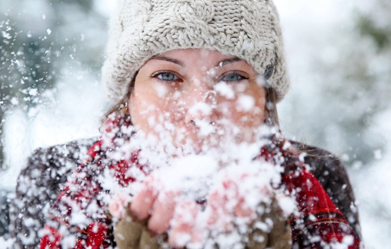 Девушка сдувает снег с ладоней